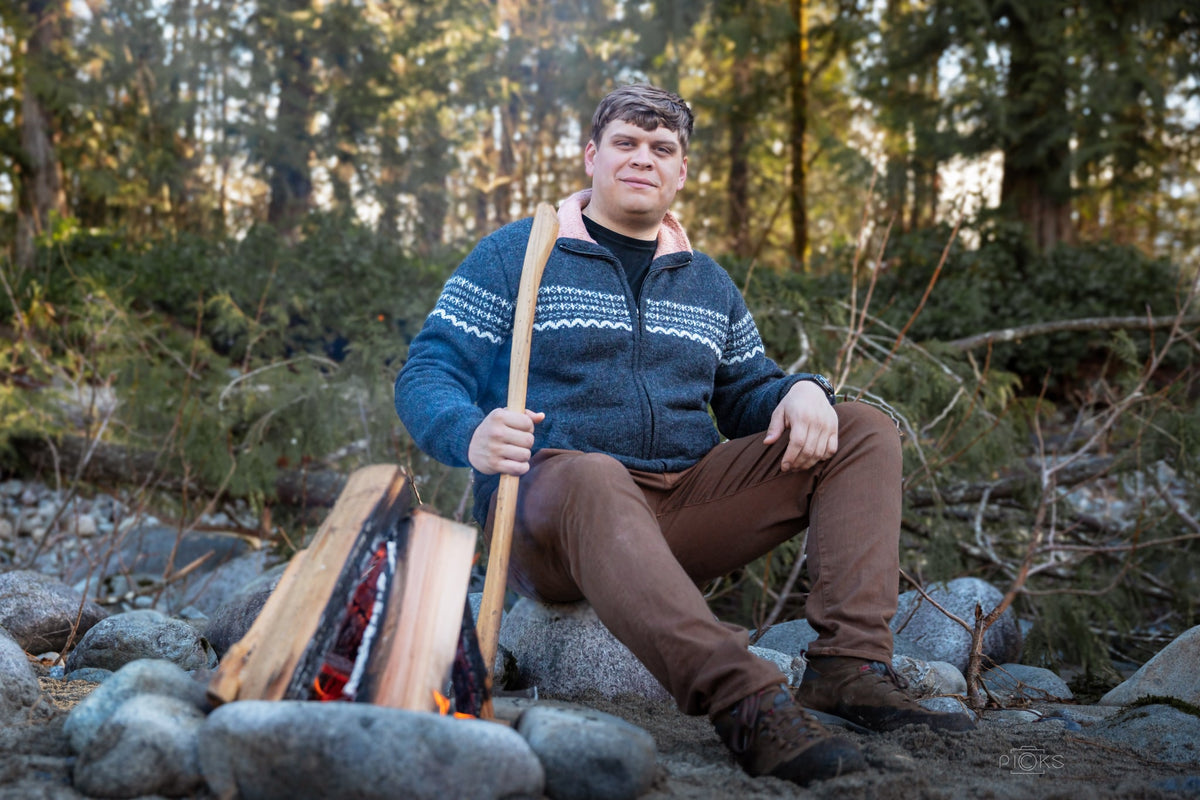 Man in a blue fleece-lined alpaca sweater seated on river rocks