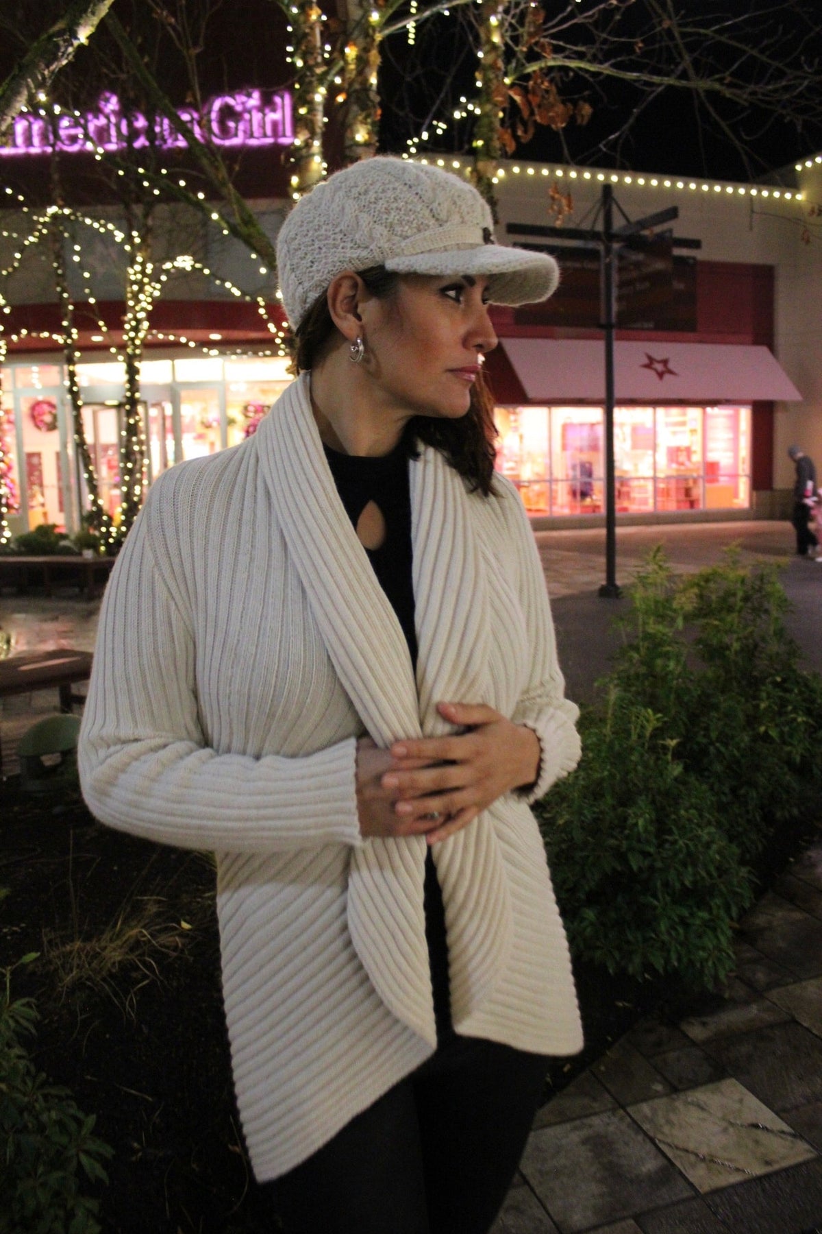 Woman in an ivory alpaca draped cardigan sweater and cap outdoors