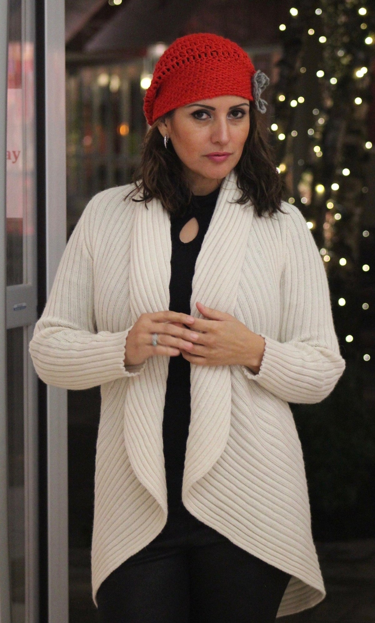 Woman in an ivory alpaca round cardigan sweater and red hat