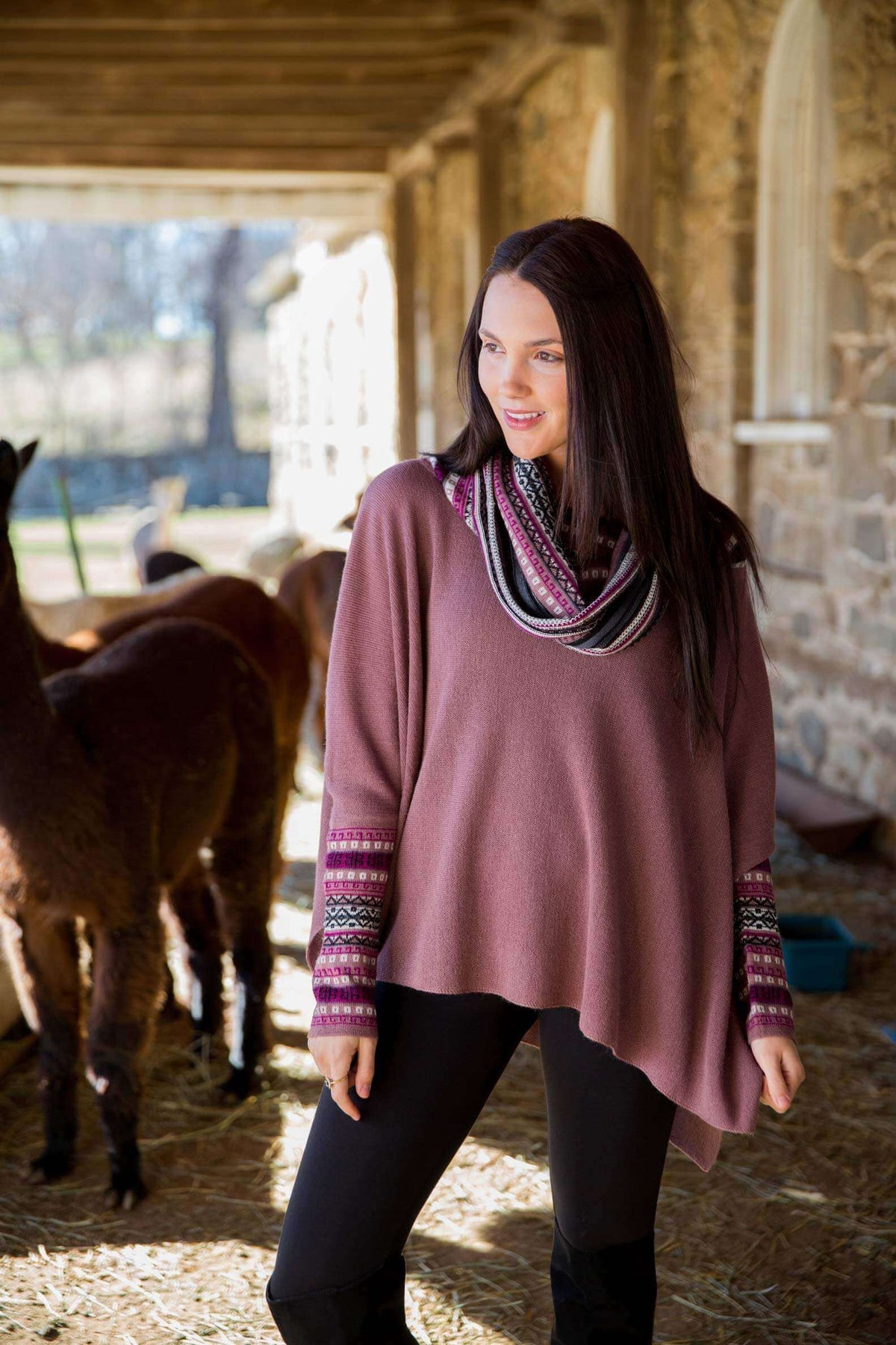 Woman in a plum alpaca poncho sweater beside alpacas