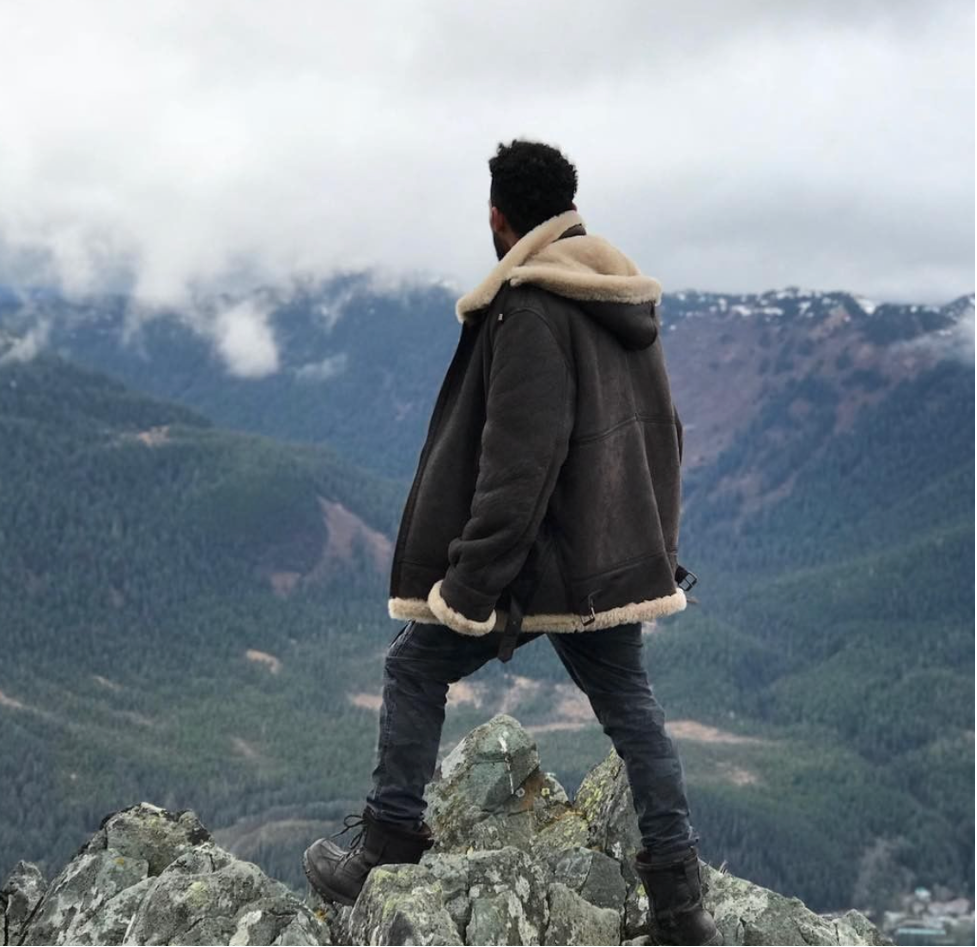 Man in a sheepskin bomber jacket overlooking a mountain valley