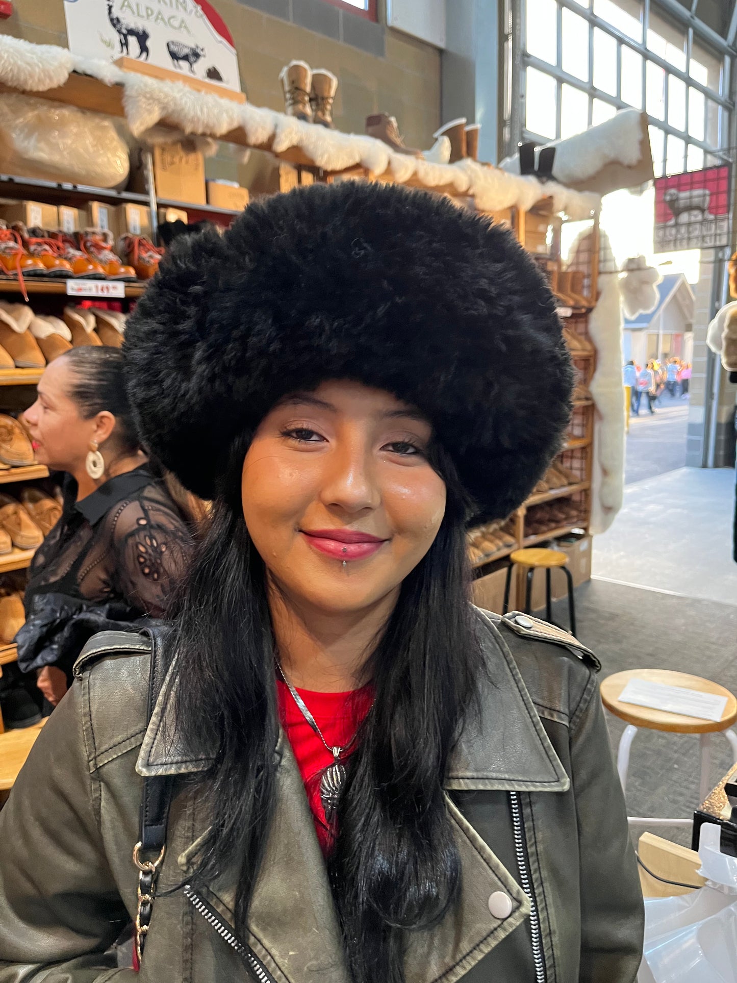 Person wearing a black fur hat and leather jacket in a store setting